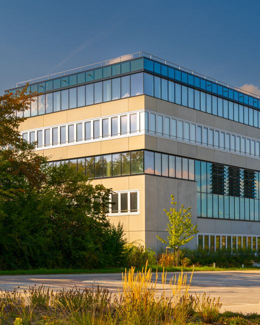 An exterior view of Stockley Park office buildings featuring modern, glass-fronted facades with metallic and concrete surfaces. The paved open area in the foreground appears clean and well-maintained,